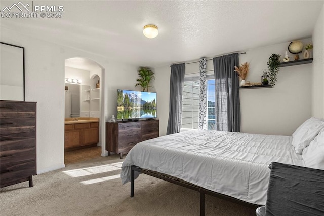 carpeted bedroom with ensuite bath and a textured ceiling