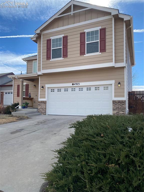 view of front of property with a garage, brick siding, fence, driveway, and board and batten siding