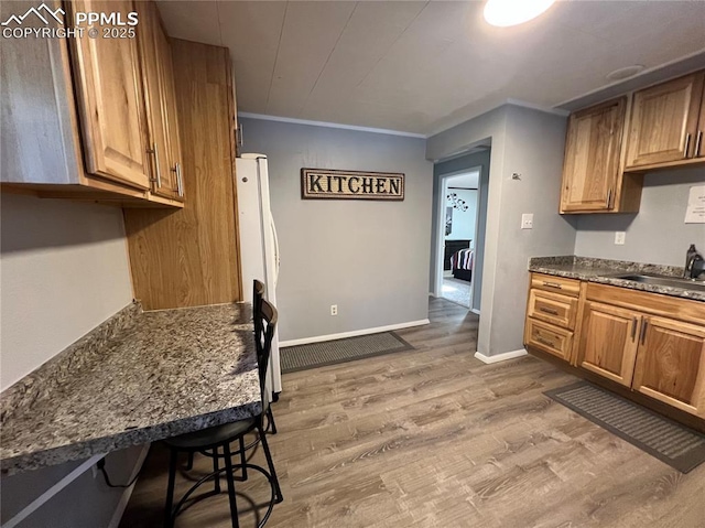 kitchen featuring sink, a breakfast bar area, white refrigerator, dark stone counters, and hardwood / wood-style floors