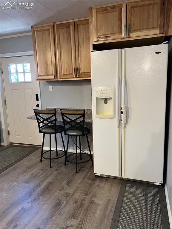 kitchen featuring crown molding, white refrigerator with ice dispenser, and dark wood-type flooring