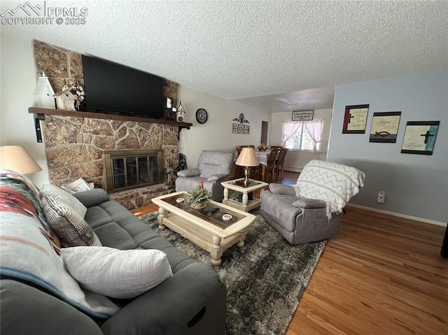 living room with hardwood / wood-style flooring, a stone fireplace, and a textured ceiling