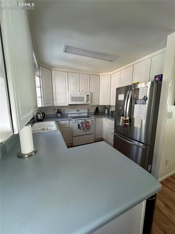 kitchen with sink, white cabinets, kitchen peninsula, dark wood-type flooring, and white appliances