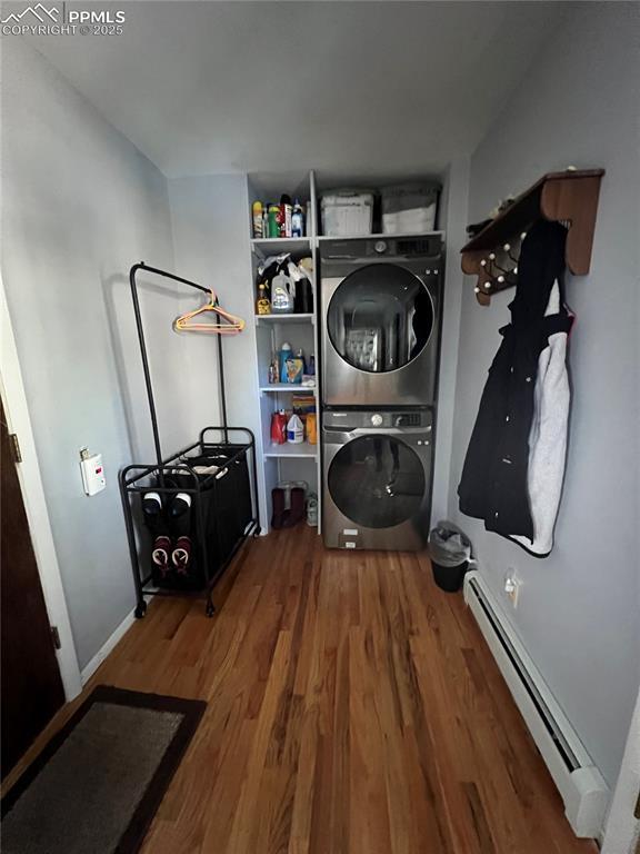 laundry area with a baseboard heating unit, hardwood / wood-style flooring, and stacked washer and clothes dryer