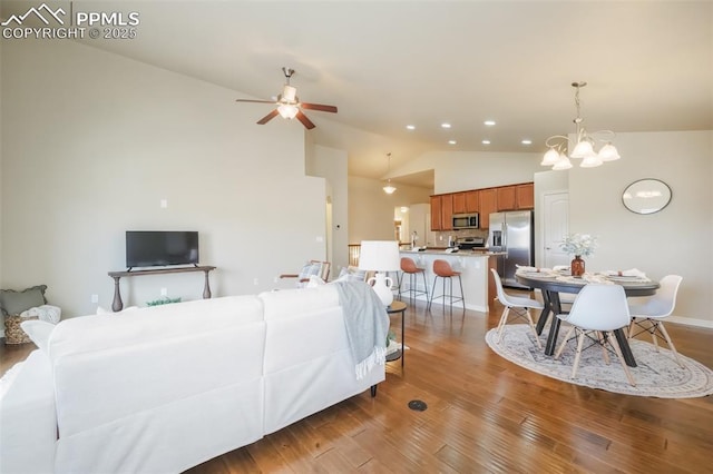 living room with high vaulted ceiling, wood-type flooring, and ceiling fan with notable chandelier