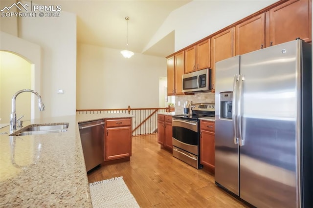 kitchen featuring pendant lighting, sink, light stone counters, light hardwood / wood-style floors, and stainless steel appliances