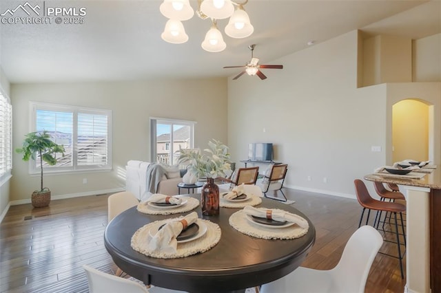 dining space featuring ceiling fan with notable chandelier, dark wood-type flooring, and high vaulted ceiling