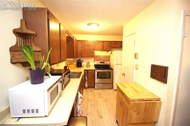 kitchen featuring white appliances, sink, light hardwood / wood-style floors, and a textured ceiling