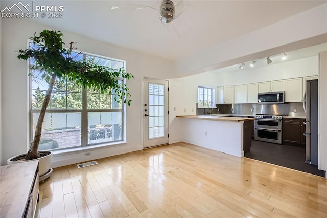 kitchen with white cabinetry, light hardwood / wood-style flooring, appliances with stainless steel finishes, kitchen peninsula, and backsplash