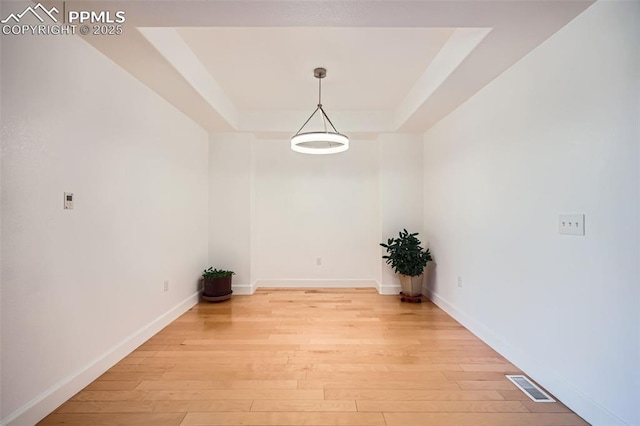 unfurnished dining area featuring a raised ceiling and light hardwood / wood-style floors