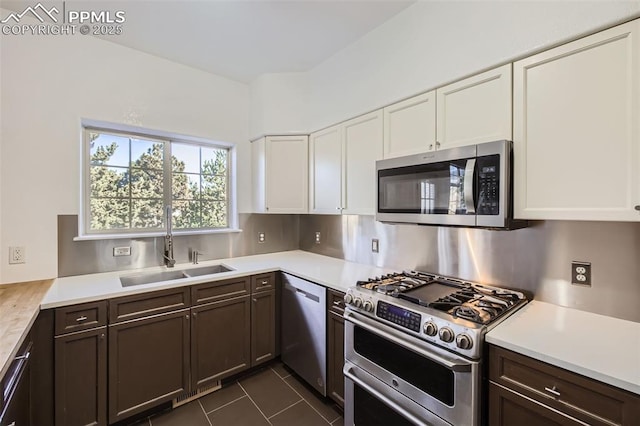 kitchen featuring sink, white cabinetry, dark brown cabinets, dark tile patterned floors, and stainless steel appliances