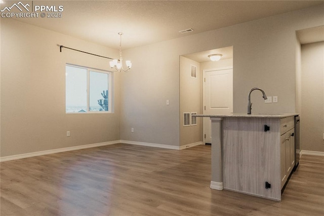 kitchen featuring sink, a kitchen island with sink, dark hardwood / wood-style floors, a notable chandelier, and decorative light fixtures