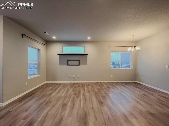 unfurnished living room featuring an inviting chandelier, wood-type flooring, and a textured ceiling