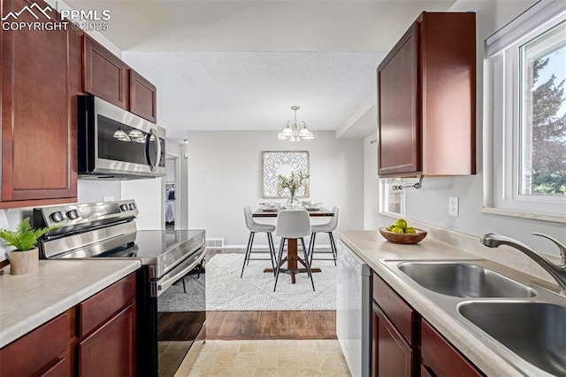 kitchen with sink, a chandelier, hanging light fixtures, a textured ceiling, and stainless steel appliances