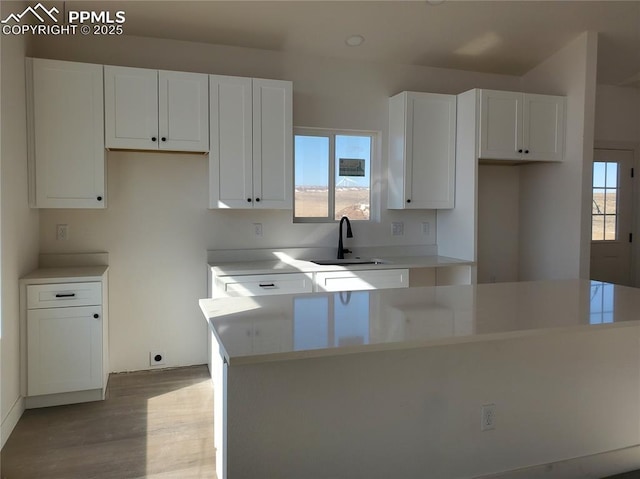 kitchen with sink, white cabinets, and light wood-type flooring