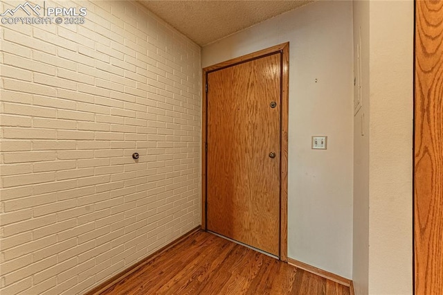 hallway featuring brick wall, hardwood / wood-style floors, and a textured ceiling