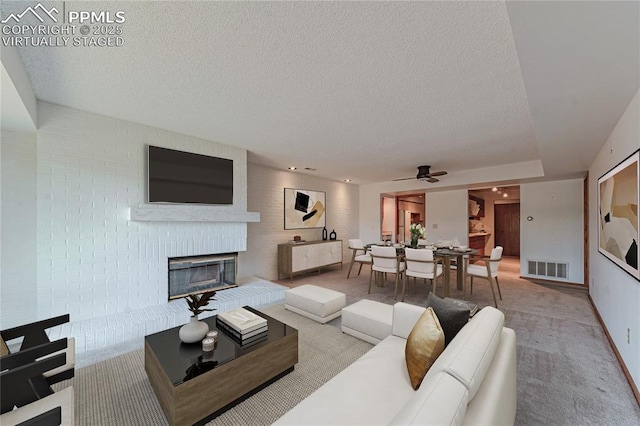 carpeted living room featuring ceiling fan, a fireplace, and a textured ceiling