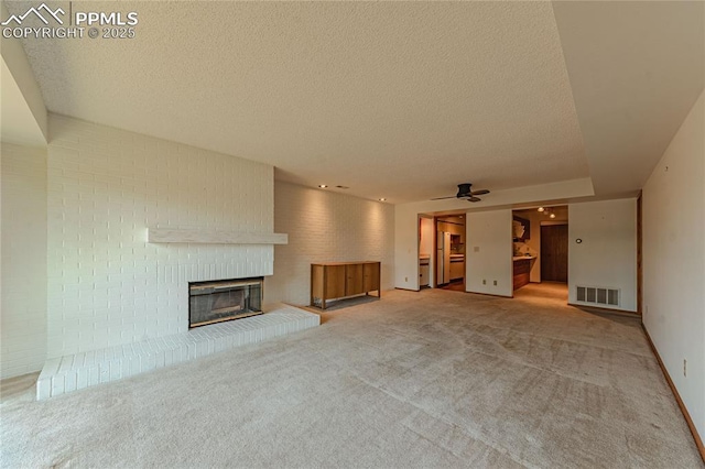 unfurnished living room with a brick fireplace, ceiling fan, a textured ceiling, and carpet