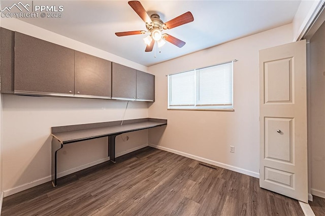 unfurnished office featuring dark wood-type flooring, built in desk, and ceiling fan