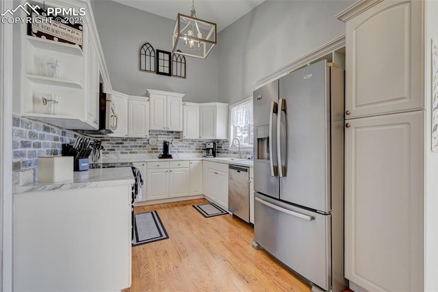 kitchen with decorative light fixtures, light wood-type flooring, white cabinets, and appliances with stainless steel finishes