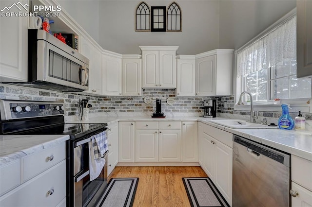 kitchen featuring sink, light hardwood / wood-style flooring, appliances with stainless steel finishes, white cabinetry, and backsplash