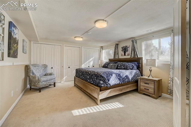 bedroom featuring two closets, light colored carpet, and a textured ceiling