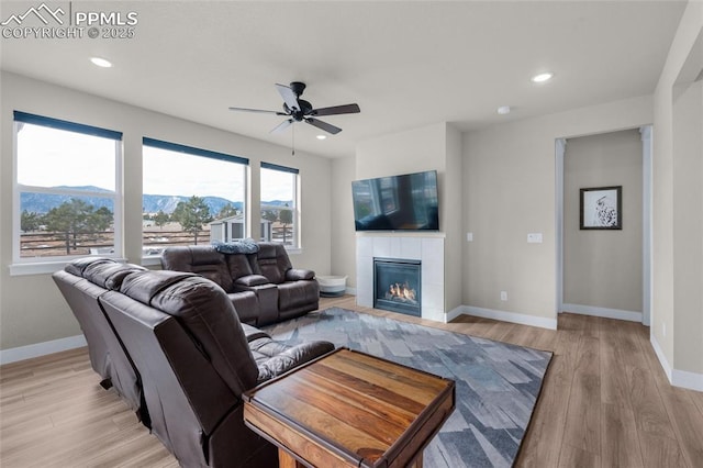 living room featuring a tiled fireplace, ceiling fan, a mountain view, and light hardwood / wood-style flooring