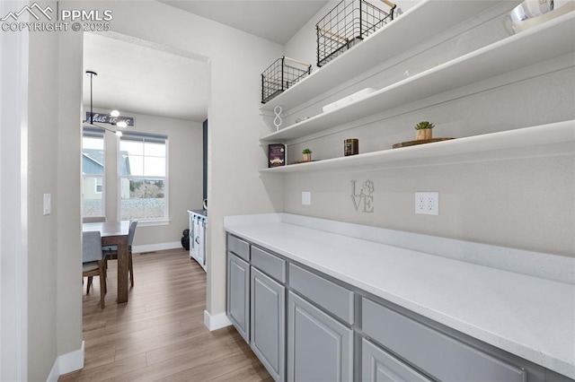 bar with an inviting chandelier, gray cabinets, and light wood-type flooring