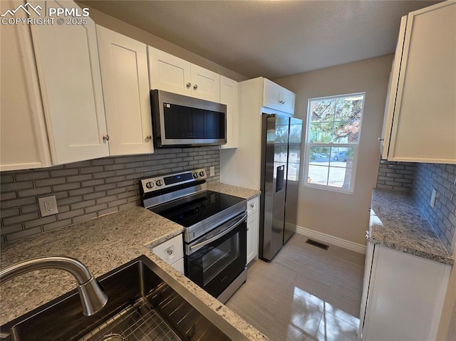 kitchen featuring stainless steel appliances, light stone countertops, sink, and white cabinets