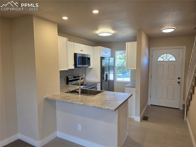 kitchen featuring sink, tasteful backsplash, kitchen peninsula, stainless steel appliances, and white cabinets