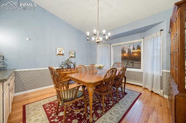 dining area featuring light wood finished floors, a wainscoted wall, lofted ceiling, and wallpapered walls