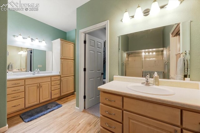 bathroom with two vanities, wood finished floors, a stall shower, and a sink