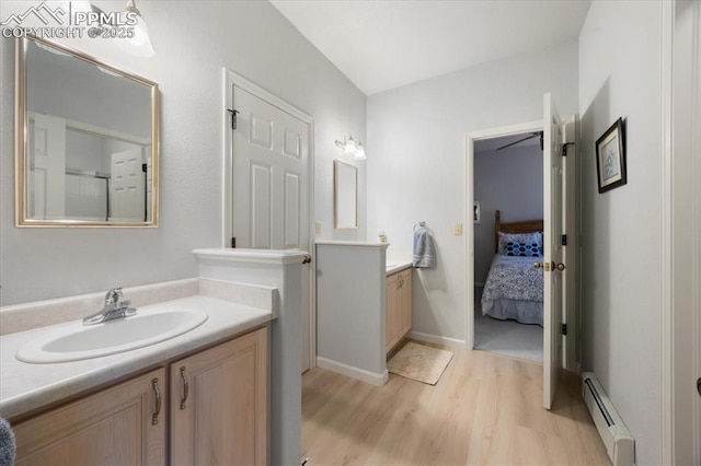 ensuite bathroom with two vanities, a sink, a baseboard heating unit, wood finished floors, and connected bathroom