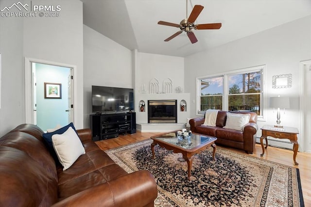 living area with a glass covered fireplace, a baseboard radiator, wood finished floors, and a ceiling fan