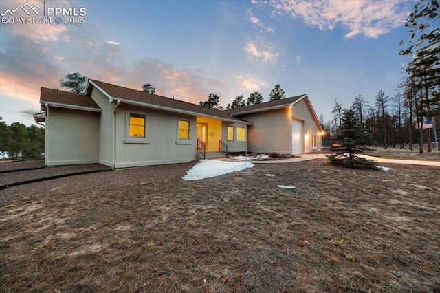 back of house at dusk with stucco siding and an attached garage