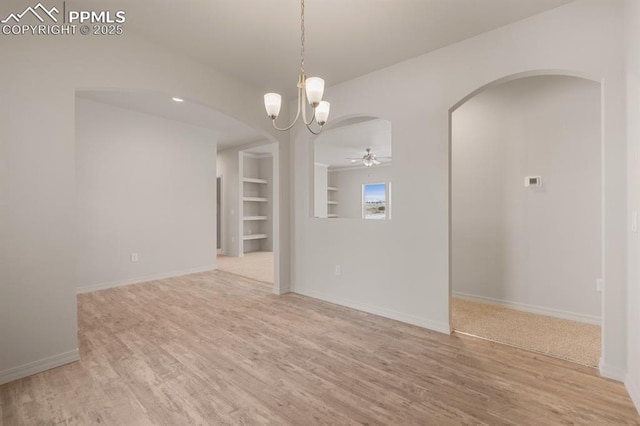 empty room featuring wood-type flooring, ceiling fan with notable chandelier, and built in features