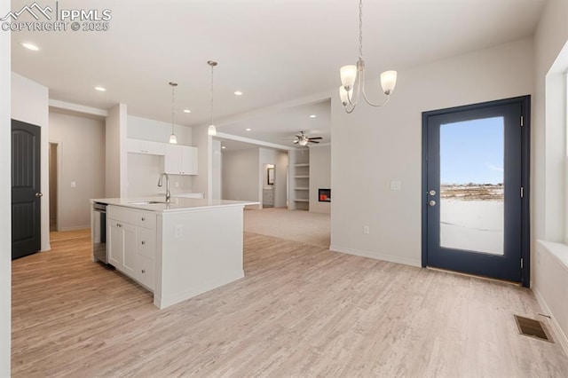 kitchen featuring decorative light fixtures, sink, white cabinets, stainless steel dishwasher, and a center island with sink