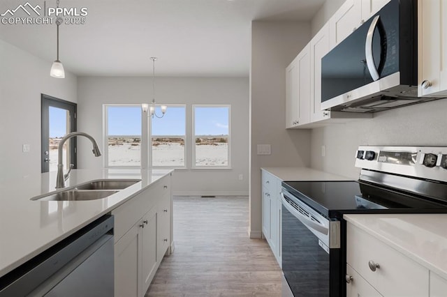 kitchen featuring decorative light fixtures, sink, white cabinets, light hardwood / wood-style floors, and stainless steel appliances