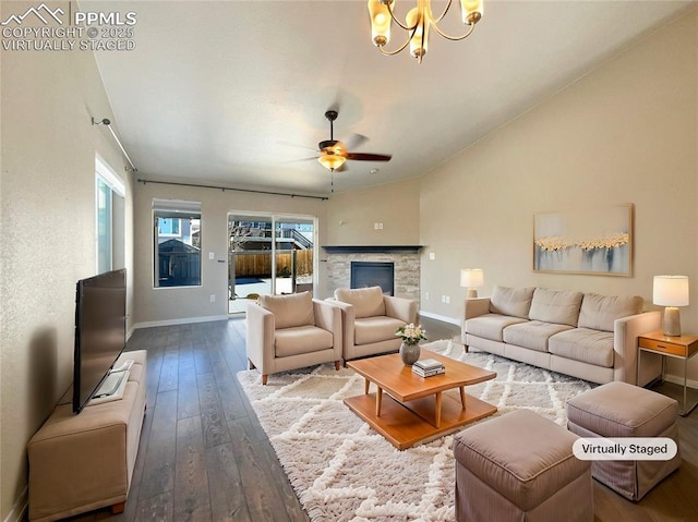 living room with lofted ceiling, ceiling fan with notable chandelier, wood-type flooring, and a stone fireplace