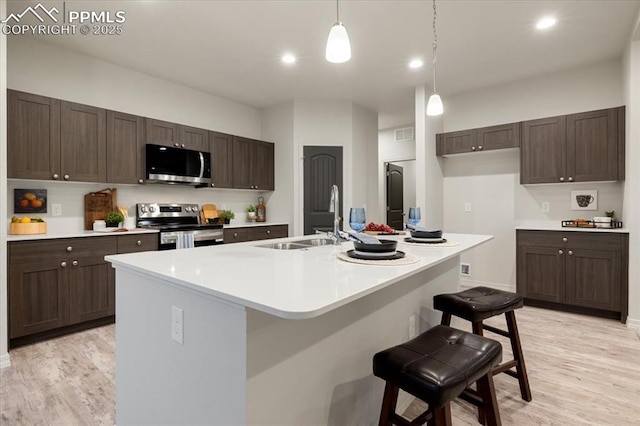 kitchen with sink, a breakfast bar area, appliances with stainless steel finishes, light hardwood / wood-style floors, and a center island with sink