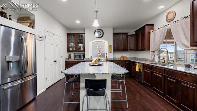 kitchen with sink, hanging light fixtures, appliances with stainless steel finishes, dark hardwood / wood-style floors, and a kitchen island