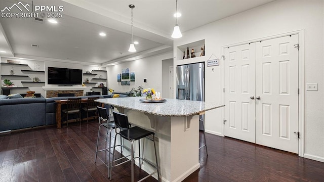 kitchen with pendant lighting, stainless steel fridge, a kitchen breakfast bar, a center island, and dark hardwood / wood-style flooring