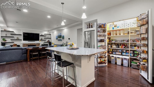 kitchen with hanging light fixtures, dark wood-type flooring, stainless steel fridge, and a kitchen bar