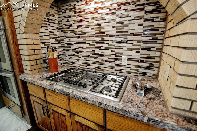 kitchen with appliances with stainless steel finishes, dark stone counters, and backsplash