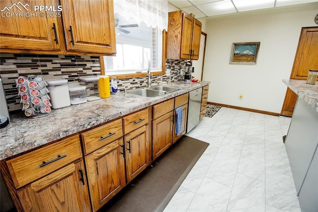 kitchen with sink, backsplash, stainless steel dishwasher, light stone countertops, and a drop ceiling