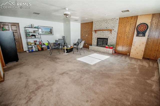 unfurnished living room with a fireplace, wooden walls, ceiling fan, and carpet flooring