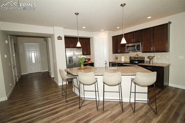 kitchen with decorative light fixtures, a center island with sink, light stone countertops, and appliances with stainless steel finishes