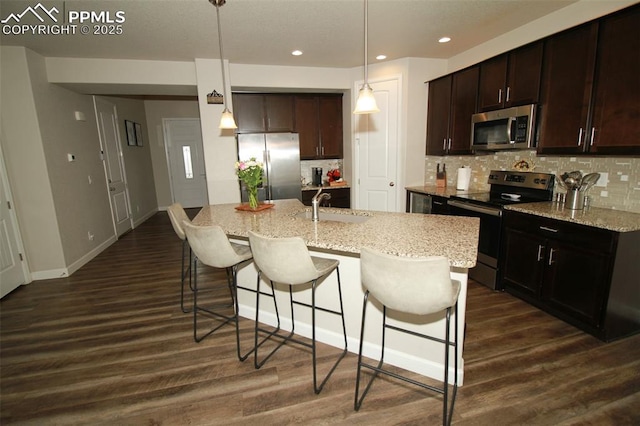 kitchen featuring appliances with stainless steel finishes, dark hardwood / wood-style floors, sink, hanging light fixtures, and a center island with sink