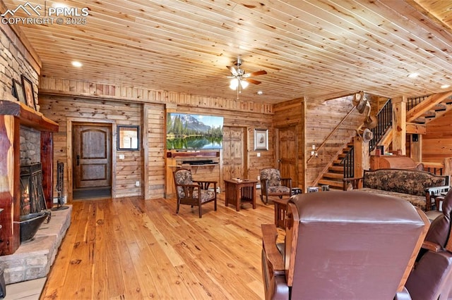 dining room featuring a stone fireplace, wood walls, ceiling fan, wooden ceiling, and light hardwood / wood-style flooring