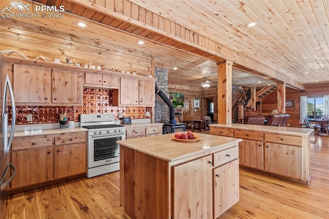 kitchen with light brown cabinetry, a wood stove, a center island, stainless steel appliances, and wooden ceiling