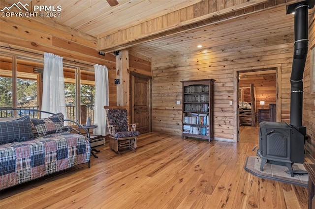 living room with wood ceiling, light hardwood / wood-style flooring, a wood stove, wooden walls, and ceiling fan